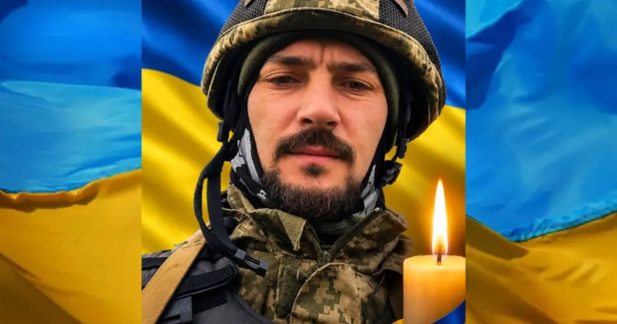 Солдат у камуфляжі та шоломі на тлі прапора України з запаленою свічкою