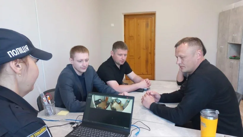 Поліцейська та троє чоловіків за столом дивляться відеодзвінок на ноутбуці