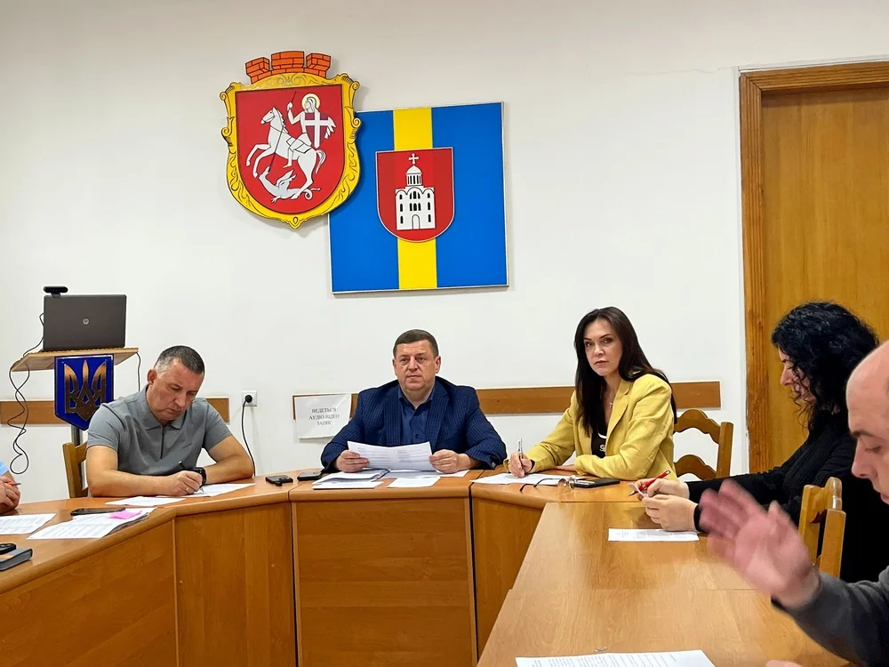Депутати за круглим столом з документами під гербами міської ради