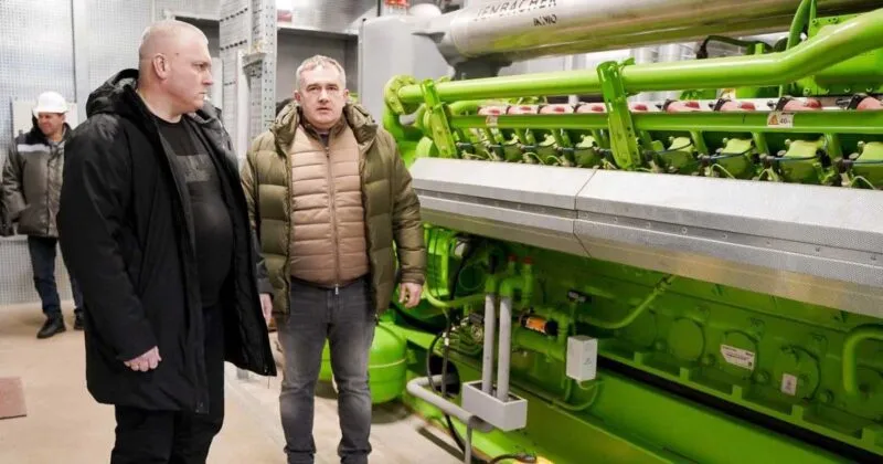 Двоє чоловіків оглядають великий зелений генератор Jenbacher у приміщенні