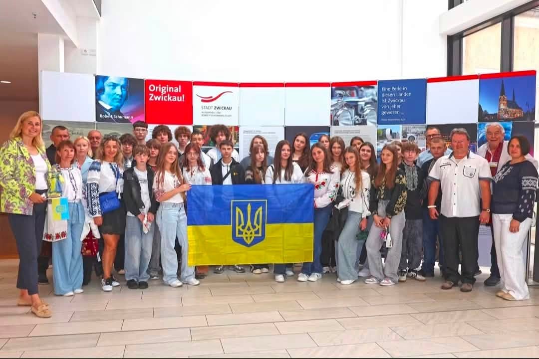 Делегація з українським прапором у залі зі стендами міста Цвіккау